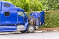 Broken blue big rig semi truck with an open hood stands in the truck stop parking lot