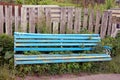 A broken blue wooden bench overgrown with grass near a gray fence Royalty Free Stock Photo