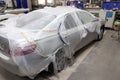 A broken car covered with a protective film from splashing paint in a spray booth in a car body repair shop before it is painted