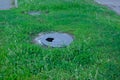 broken cast-iron manhole among the grass in park. Manhole with a hole