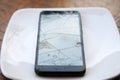 Broken Cellular Telephone. A Cellular Telephone with a cracked and broken Screen on a white plate on a table. Broken Cell Phone Royalty Free Stock Photo