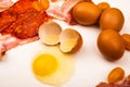 Broken chicken egg and scattered eggs, sliced sausage and bacon, tomatoes on a white background. Close up Royalty Free Stock Photo