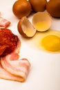 Broken chicken egg and scattered eggs, slices of sliced sausage and bacon on a white background. Close up Royalty Free Stock Photo