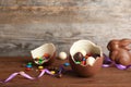 Broken chocolate Easter egg with candies on wooden table. Royalty Free Stock Photo