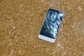 Broken crashed smartphone is lying in the water. Phone in the sandy beach Royalty Free Stock Photo