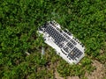 A broken and discarded computer keyboard is buried in the grass