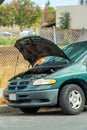 Broken down car engine with hood up on the side of street or road in an urban or industrial area needing mechanic and repairman
