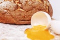 Broken egg on a floured wooden board on a background of appetizing fresh round bread. Homemade baking. Close-up Royalty Free Stock Photo