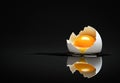 Broken eggshell with raw egg on a black minimalist surface reflective background Royalty Free Stock Photo