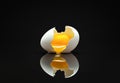 Broken eggshell with raw egg on a black minimalist surface reflective background Royalty Free Stock Photo