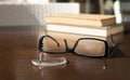 a broken eyeglass frame lies in front of a stack of old books on a brown table Royalty Free Stock Photo