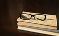 a broken eyeglass frame lies on a stack of old books on a brown wooden table Royalty Free Stock Photo