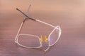 Broken eyeglasses lying on a brown wooden surface.Damaged bridge of eyeglasses.Selective focus.Maintenance and repair concept