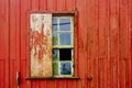 Broken glass and wood window from abandoned house facade with old peeling red wooden wall and grungy surface texture