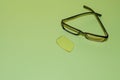 Broken glasses with a fallen lens and crossed arms lie on a green surface. Nearby is a yellow lens. View from above Royalty Free Stock Photo