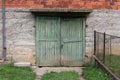 Broken green wooden garage doors with rusted metal hinges and small door handle mounted on concrete wall of red bricks house