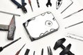 Broken HDD, harddisk in middle of white bakground. Various tools around bulb, clamp, brush,file,pincers,hammer etc. Symbol of