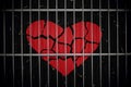 Broken heart paper cutout behind metal bars in black background. Royalty Free Stock Photo