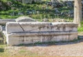 Broken long marble piece of a building carved with Roman letters stacked beside ruins at anicent Corinth near the Temple of Apollo