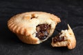 Broken open traditional british christmas mince pie with fruit filling isolated on black slate