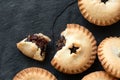 Broken open traditional british christmas mince pie with fruit filling next to whole mince pies on black slate. Top view. Copy