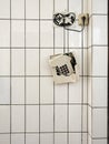 A broken phone hangs by its cord in front of a white tiled wall in an old building Royalty Free Stock Photo