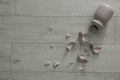 Broken pink ceramic vase on wooden floor, flat lay. Space for text Royalty Free Stock Photo