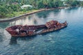 Broken rusty boat in water near tropical shore against of palm trees and forest. Sanma, Vanuatu
