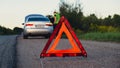 Broken silver luxury car emergency accident. Man driver installing red triangle stop sign on road. Sport automobile Royalty Free Stock Photo