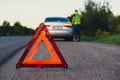 Broken silver luxury car emergency accident. Man driver installing red triangle stop sign on road. Sport automobile Royalty Free Stock Photo