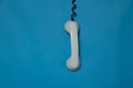 broken telephone receiver on wire weighs on blue isolated background, telephone receiver on prododi is broken Royalty Free Stock Photo