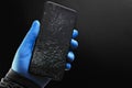 A broken touch phone with a cracked screen in your hand on a black background. Royalty Free Stock Photo