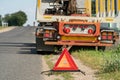 A broken truck is standing on the side of the road waiting for a tow truck. A red emergency stop sign stands on the road in front