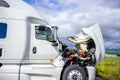 Broken white big rig semi truck tractor stands on the side of the road with an open hood awaiting mobile repair assistance Royalty Free Stock Photo