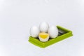 Broken and whole white eggs on green kitchen cutter on a white surface Royalty Free Stock Photo