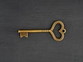 Bronze antique key with heart shaped hole on black wooden background Royalty Free Stock Photo