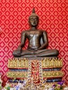 Bronze Buddha statue with red wall behind in the temple. Royalty Free Stock Photo