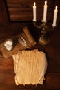 Bronze candlestick with three burning candles on a wooden brown table. Old parchment with goose feather.