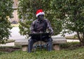 Bronze of a man sitting on a stone bench, writing, decorated with a removable Santa Hat at Christmas in Dallas, Texas