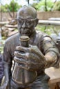 Bronze sculpture of an elderly man holding a container in his hands