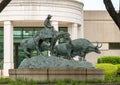 Bronze sculpture by unidentified artist featuring a cowboy on a horse herding cattle.