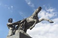 Bronze sculpture of young man taming horse at an Anichkov bridge in St. Petersburg against the blue sky with light clouds