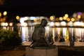 Bronze statue of a boy with a lake and the city lights in the background at night in Stavanger.