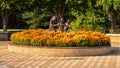 Bronze statue of a boy and two girls happily dancing in a circle in a bed of orange flowers in Irving, Texas.