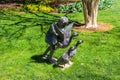 A bronze statue of a child holding a duck surrounded by colorful flowers and lush green trees and plants