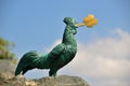 The bronze statue of a cock with golden cloverleaf in its beak.