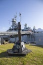 A bronze statue of a man holding up his right hand in front of the USS Alabama ship surrounded by lush green grass with blue sky