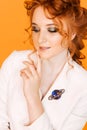 Brooch in the shape of a planet with a ring on the white jacket of a red-haired girl. Girl posing on orange background Royalty Free Stock Photo