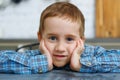 A brooding blond boy sits at the kitchen table and stares at the camera. A large portrait of a child with his hands in his face Royalty Free Stock Photo