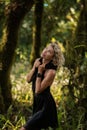 Brooding dreamy young girl blonde, black dress with a hood standing by a tree Royalty Free Stock Photo